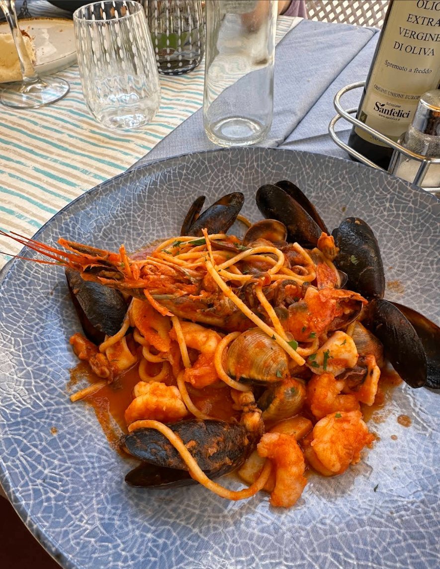Tavolo apparecchiato all'aperto con pasta allo scoglio, acqua e olio del Garda